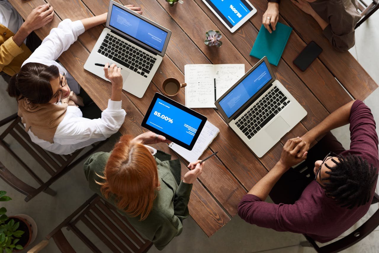 Home Diverse team discussing business strategies with laptops and tablets at a wooden table.